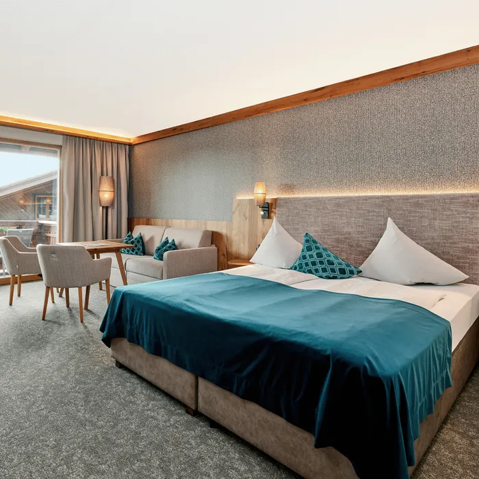 Moderna camera d'albergo con letto matrimoniale, area salotto e accesso al balcone